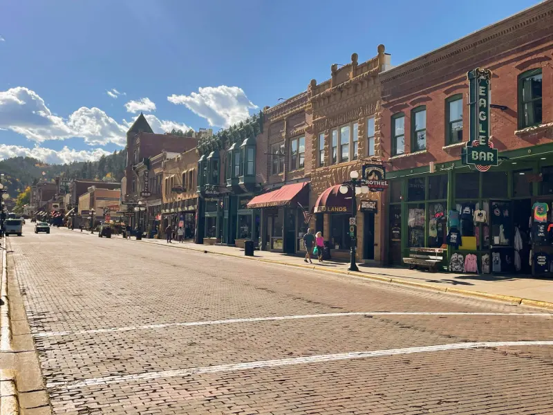 Deadwood's Main Street, paved in brick and lined with restored brick and sandstone buildings, with fall color on the hills behind.
