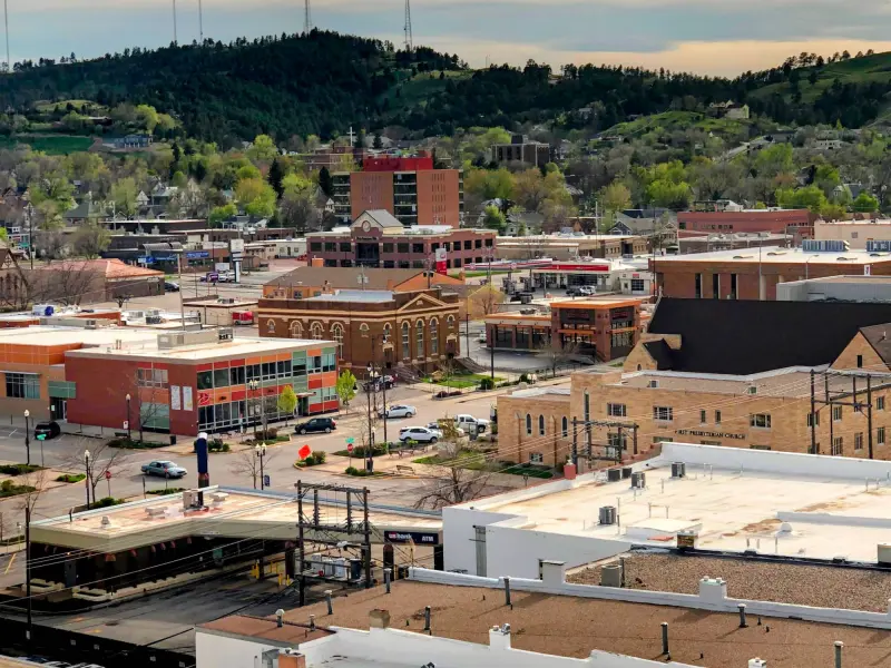 Downtown Rapid City seen from above, brick buildings and First Presbyterian Church in front of pine-covered hills.